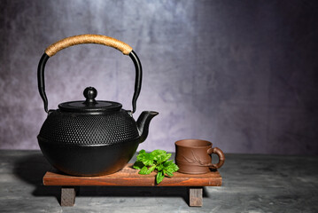 Traditional Asian cast-iron kettle with clay cup on a wooden stand.
