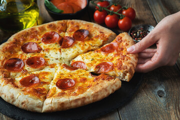 A slice of hot Italian pizza with stretching cheese. Pizza pepperoni on a dark wooden background