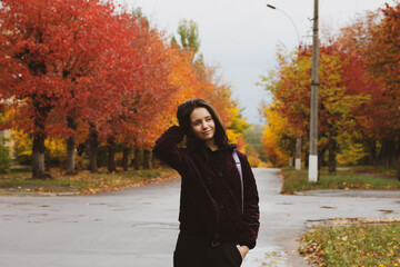 Stylish school girl on a street. Red, yellow trees in fall season Young woman portrait outdoors in autumnal day. People on nature in October. Teens on the holidays. University campus, travel lifestyle