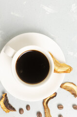Mushroom coffee in a white cup and saucer with dried mushrooms and coffee beans. The concept of a trendy beverage. The drink is good for health. Vertical orientation. Selective focus. Top view