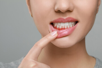 Woman showing inflamed gum on grey background, closeup