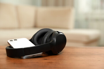 Modern wireless headphones and smartphone on wooden table indoors, space for text