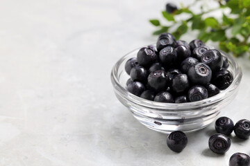 Ripe bilberries in bowl on light marble table, closeup. Space for text