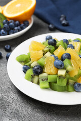 Plate of tasty fruit salad on grey textured table, closeup