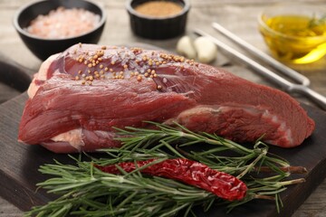 Piece of raw beef meat, rosemary, spices and chili pepper on table, closeup