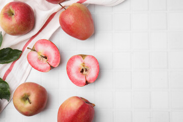 Tasty apples with red pulp and leaves on white tiled table, flat lay. Space for text