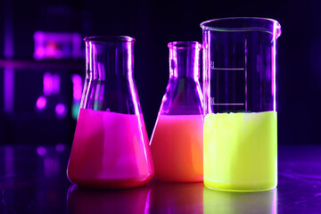 Laboratory glassware with luminous liquids on table against dark background