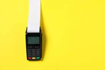 Payment terminal with thermal paper for receipt on yellow background, top view. Space for text