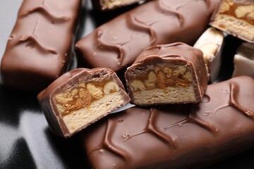 Tasty chocolate bars with nougat and nuts on black plate, closeup
