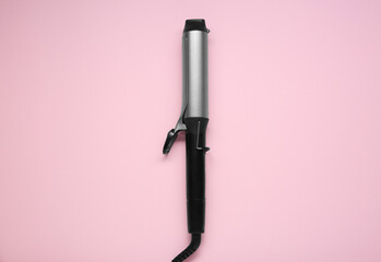 Hair styling appliance. One curling iron on pink background, top view