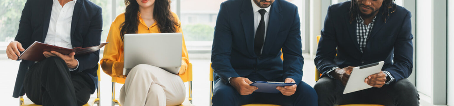Diversity candidates siting while waiting for job interview in front view. Low section crop of interviewees sitting on a chair while preparing their document and holding their laptop. Intellectual.