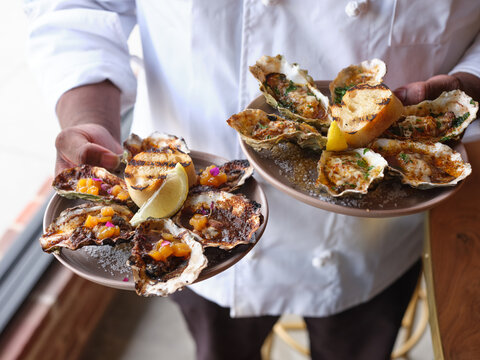 Person holding plates of grilled oysters.