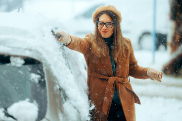 Woman with a Brush Removing snow from her Car After Blizzard. Person using a snow broom to uncover...