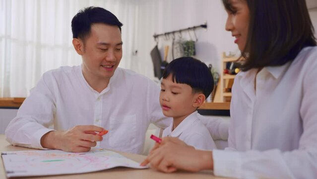 Adorable Asian young son draw picture on paper with parents in house.