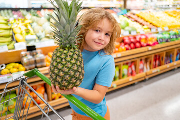 Happy little kid with fruits and vegetables at grocery store. Healthy food for young family with kids. Happy child with shopping cart full of fresh vegetables. Kids at grocery store or supermarket.