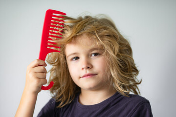 Kids hair. Funny child with curly blonde hair holding comb hairbrush for combing. Kid hair care. Little kid combing hair, isolated studio background. - obrazy, fototapety, plakaty