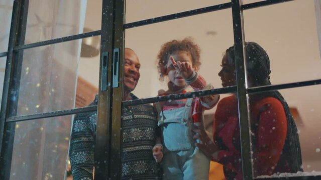 Adorable child looking at the window and first snow flakes with family.