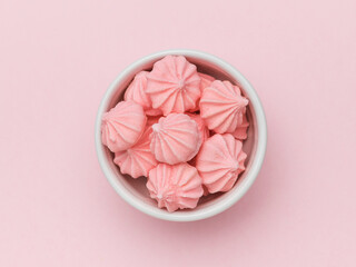 Top view of pink meringue in a white bowl on a pink background.