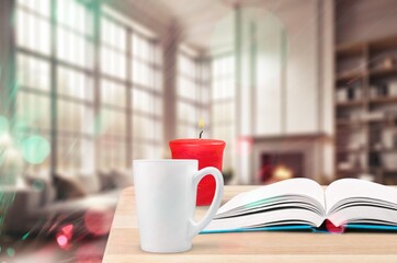 Coffee cup and burning candle on table in bedroom.