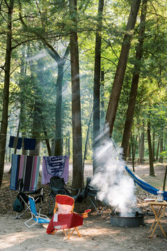 A vertical image of a peaceful campsite with lawn chairs, campfire, and hammock in the forest. 