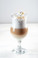 Cappuccino with whipped cream and almonds in a glass mug on a white background