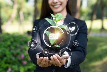 Focused young plant on soil with ESG and eco friendly icon design holding by blurred businesswoman...