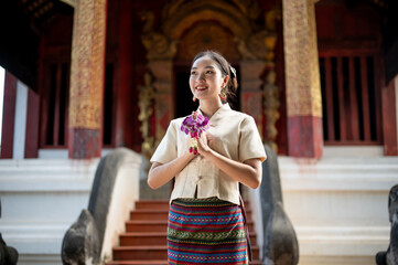 A beautiful Thai woman is standing in a temple in a prayer position with a garland in her hands.