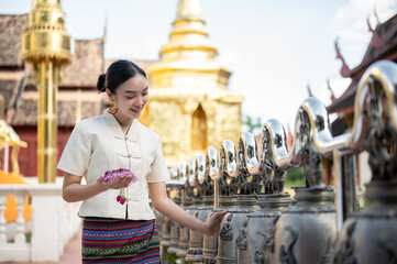 Beautiful Thai-Asian woman in a traditional Thai-Northern dress is ringing temple bells in a temple.