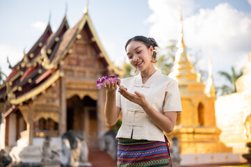 A charming Thai woman in a traditional Thai-Lanna dress is admiring a beautiful garland in her hand.