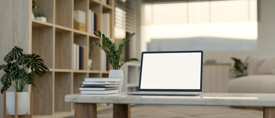 A laptop, books, and a ceramic vase on a coffee table in a modern, minimalist home living room.