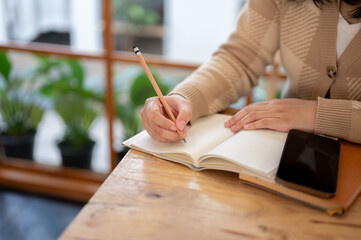 Close-up image of a woman writing something or taking notes in her book at a table in a cafe.
