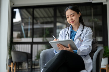 A beautiful Asian female doctor is working on her digital tablet, reading medical cases online