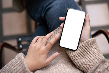 Close-up image of a woman in casual clothes is using her smartphone while sitting outdoors.
