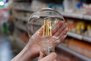 Large transparent lamp with filament diodes in female hands.