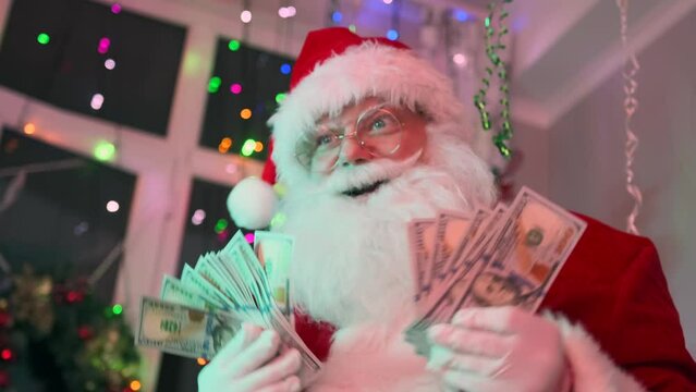 Rich Santa is having a blast at party with pile money bills in hands and dollars pouring down on him, dancing against the backdrop of festive colorful garlands and Christmas decorations. Xmas time.