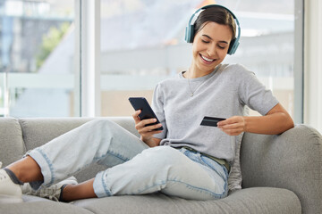 Obraz premium Sofa, headphones and phone with credit card and woman at home with purchase, music and smile. Online shopping, tech and internet with banking and audio with mobile by a sofa with digital buying