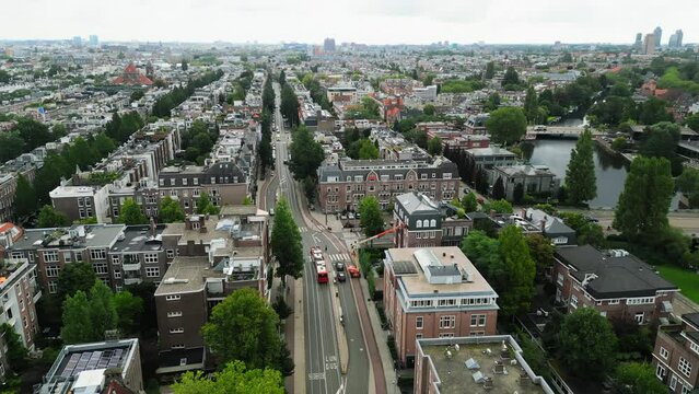Scenic drone footage of lines of residential buildings and streets with low traffic, green old-growth trees rising majestically and canal in the distance. High quality 4k footage