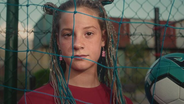 Sporty adolescent with dyed afro braids spends free time posing for camera after impromptu match. Confident girl goalkeeper with determined look demonstrates love for sport on football pitch