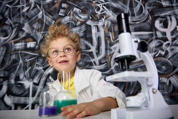 Boy with hair on end and a white coat dreams of incredible discoveries while doing chemistry. An...