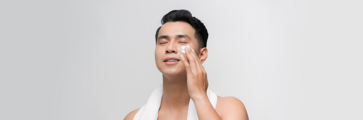 Young asian man applies moisturizer on his face. Male skin care.