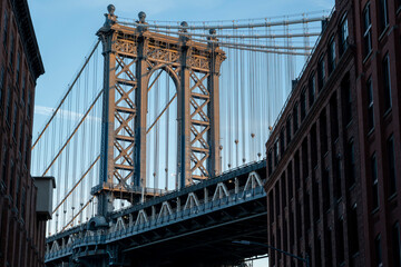 Manhattan Bridge between Manhattan and Brooklyn over East River seen from a narrow alley enclosed by two brick buildings on a sunny morning in Washington street in Dumbo, Brooklyn, NYC