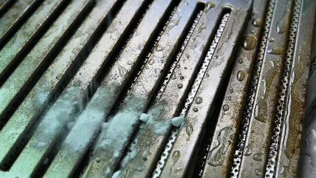 Housekeeping pouring baking soda on the surface of stained cooker hood filters at kitchen sink before cleaning it.