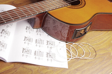 Classical guitar and book of guitar chords on a wooden table.