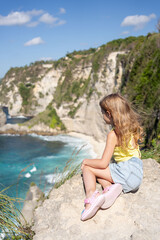 Back view child girl on the edge of a cliff looking at Diamond beach, Nusa Penida. Scenic view of Diamond Beach in Nusa Penida Bali, Indonesia.