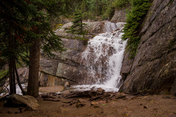 A high mountain waterfall in the middle of a coniferous forest and the slopes of the Rocky...