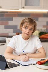 Beautiful woman writing on a piece of paper at the table in the kitchen