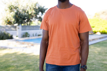 Mid section of african american man in orange t-shirt with copy space in garden
