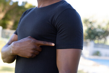 African american man in black t-shirt pointing at sleeve with copy space in garden