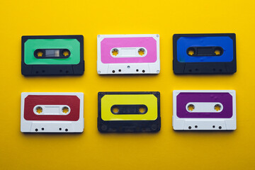 Overhead view of six colourful cassette tapes arranged on yellow background