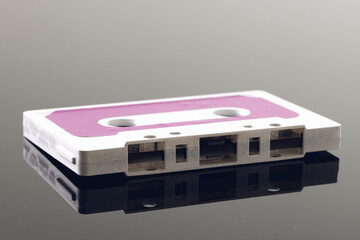 Close up of white and pink cassette tape on grey background with reflection